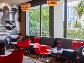 Un espace repas moderne avec des chaises rouges, des tables noires et une vue sur la verdure environnante.