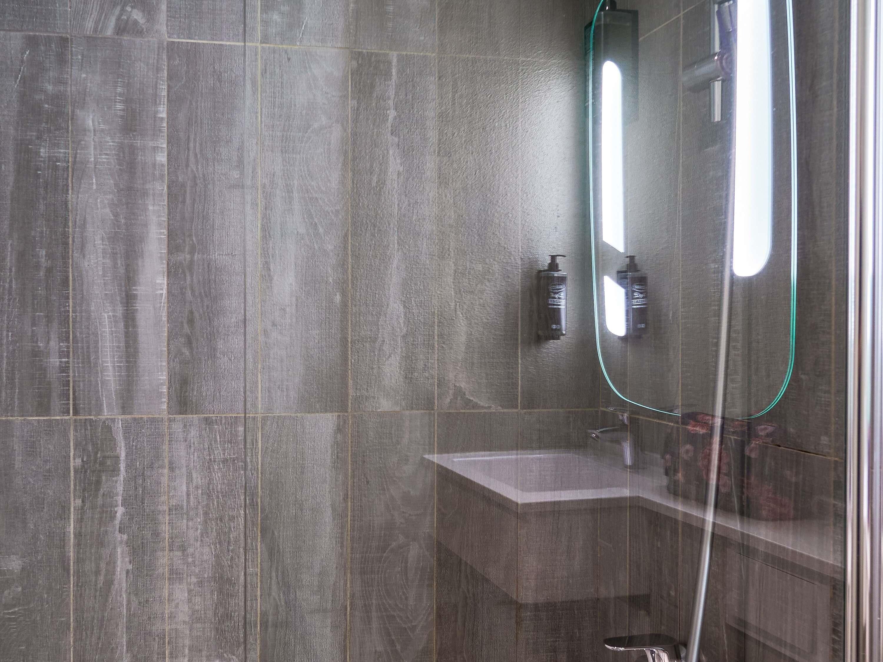 A modern bathroom with a large mirror, a handheld showerhead, and a sink.