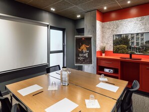 Une salle de conférence équipée d’une grande table, de chaises, d’un tableau blanc, d’une affiche et d’un téléviseur.