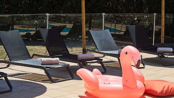 Des fauteuils de jardin et un flamant rose gonflable décoratif sur une terrasse carrelée.