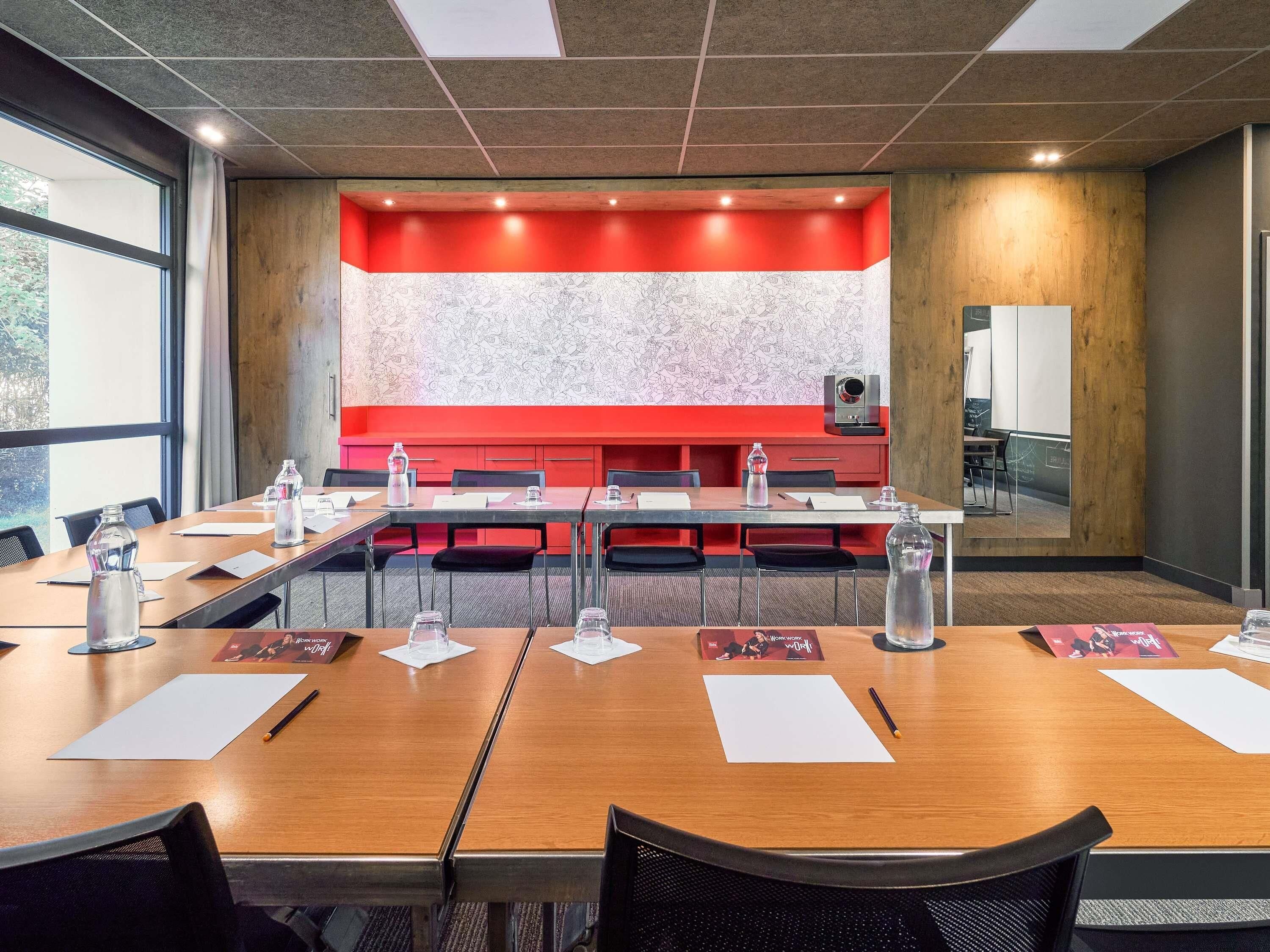 Un salón de conferencias con una larga mesa, sillas, botellas de agua y un proyector.