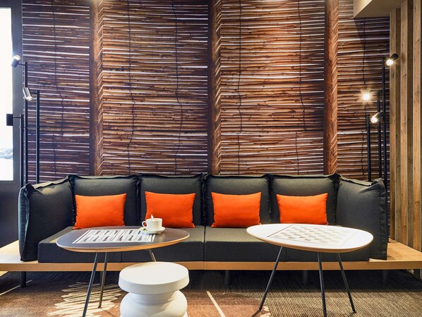 A modern interior with a black sofa, orange cushions, and two round tables with menus. - ibis Toulon La Seyne Sur Mer (La Seyne-sur-Mer)