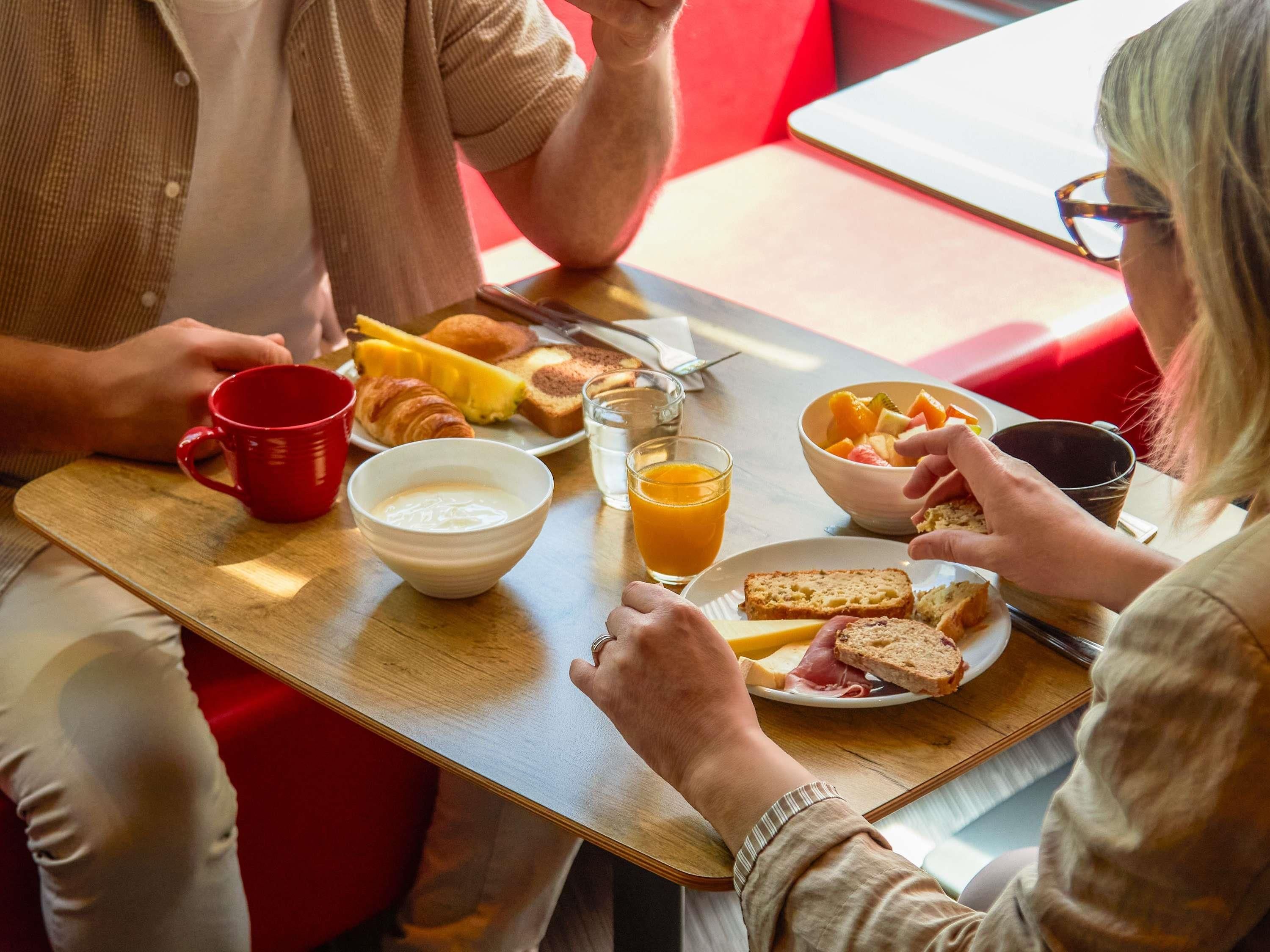 Una mesa para comer con alimentos para el desayuno, una taza roja y un vaso de jugo de naranja.