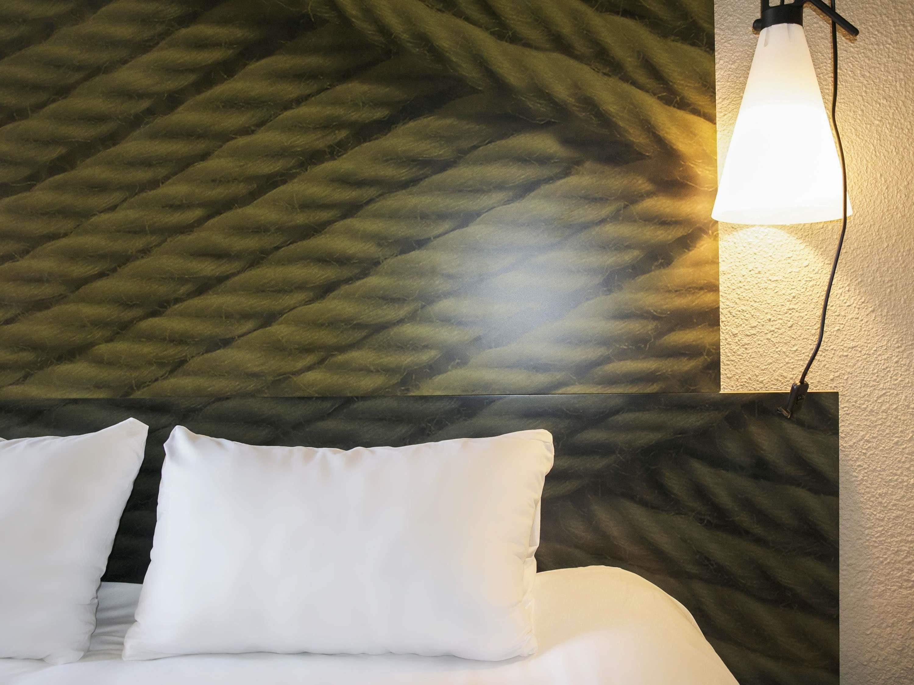 A bed with white bedding, a textured wall behind it, and a wall-mounted light fixture.