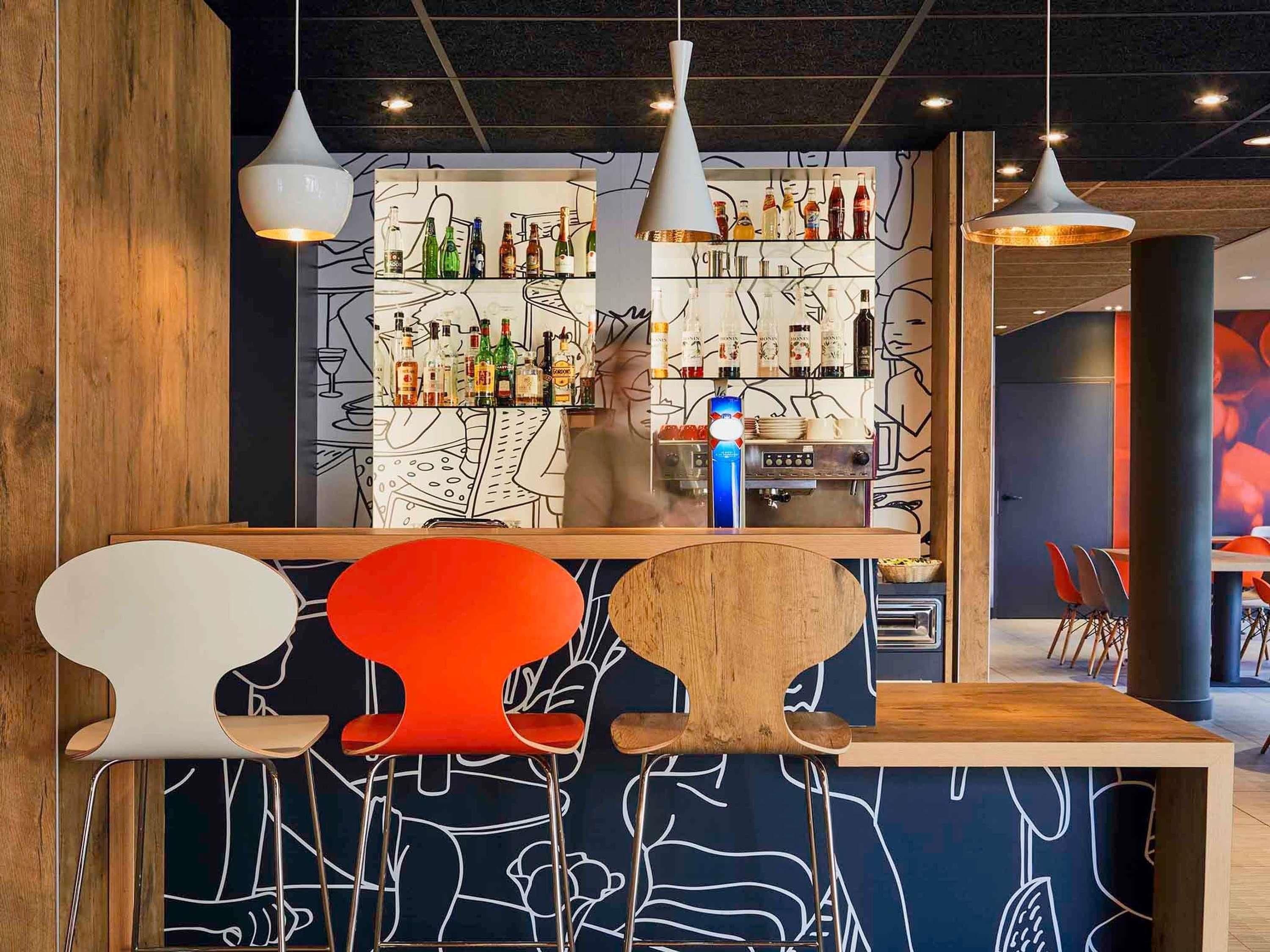A bar area with a wooden counter, modern chairs, and a wall decorated with bar bottles and abstract art.