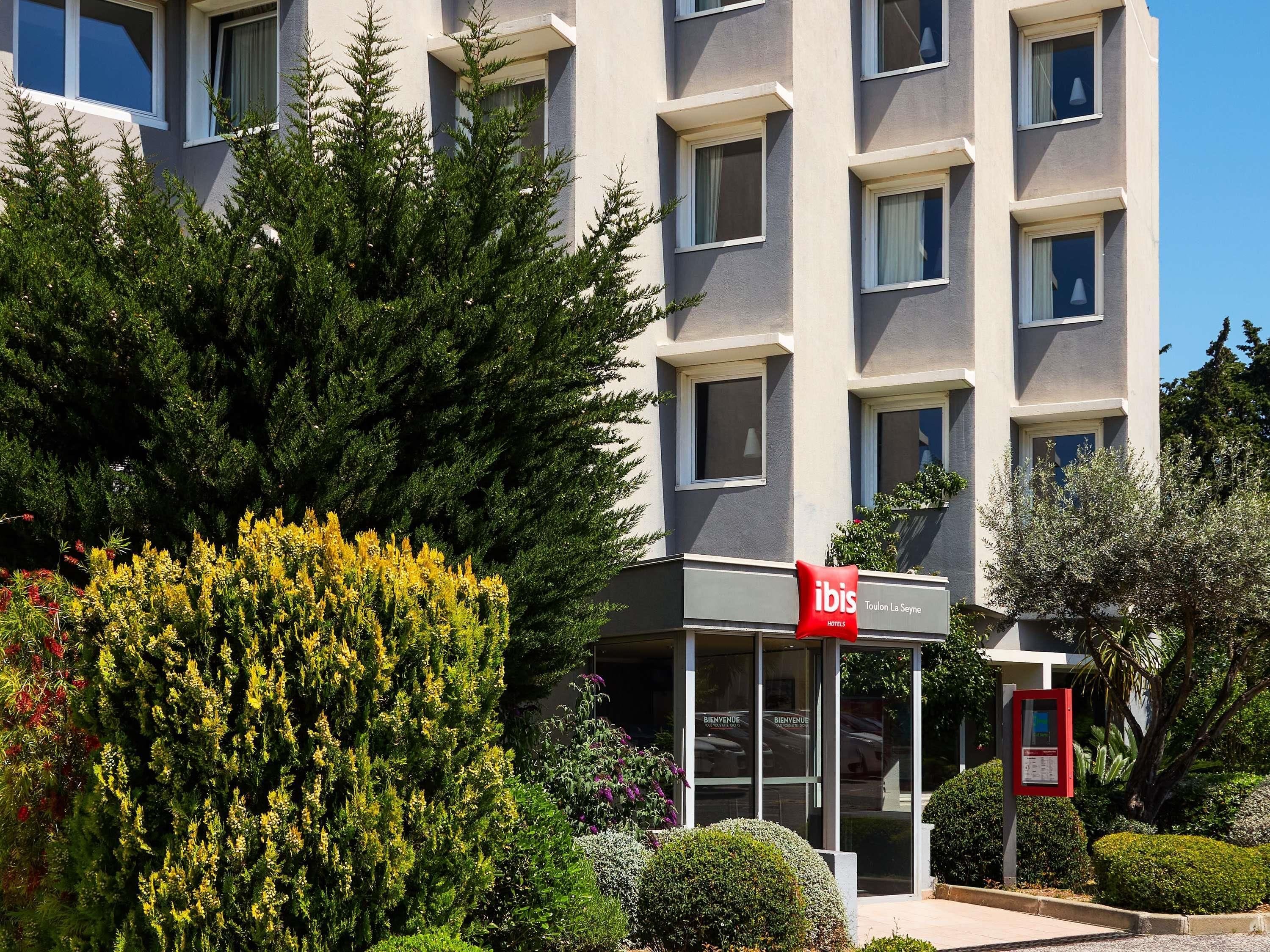 Un bâtiment d'hôtel avec de nombreuses fenêtres, une enseigne rouge et de la verdure environnante.