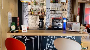 A bar area with shelves of bottles, a coffee machine, and a counter with a neon sign. - ibis Toulon La Seyne Sur Mer (La Seyne-sur-Mer)