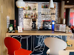 A bar area with shelves of bottles, a coffee machine, and a counter with a neon sign. - ibis Toulon La Seyne Sur Mer (La Seyne-sur-Mer)