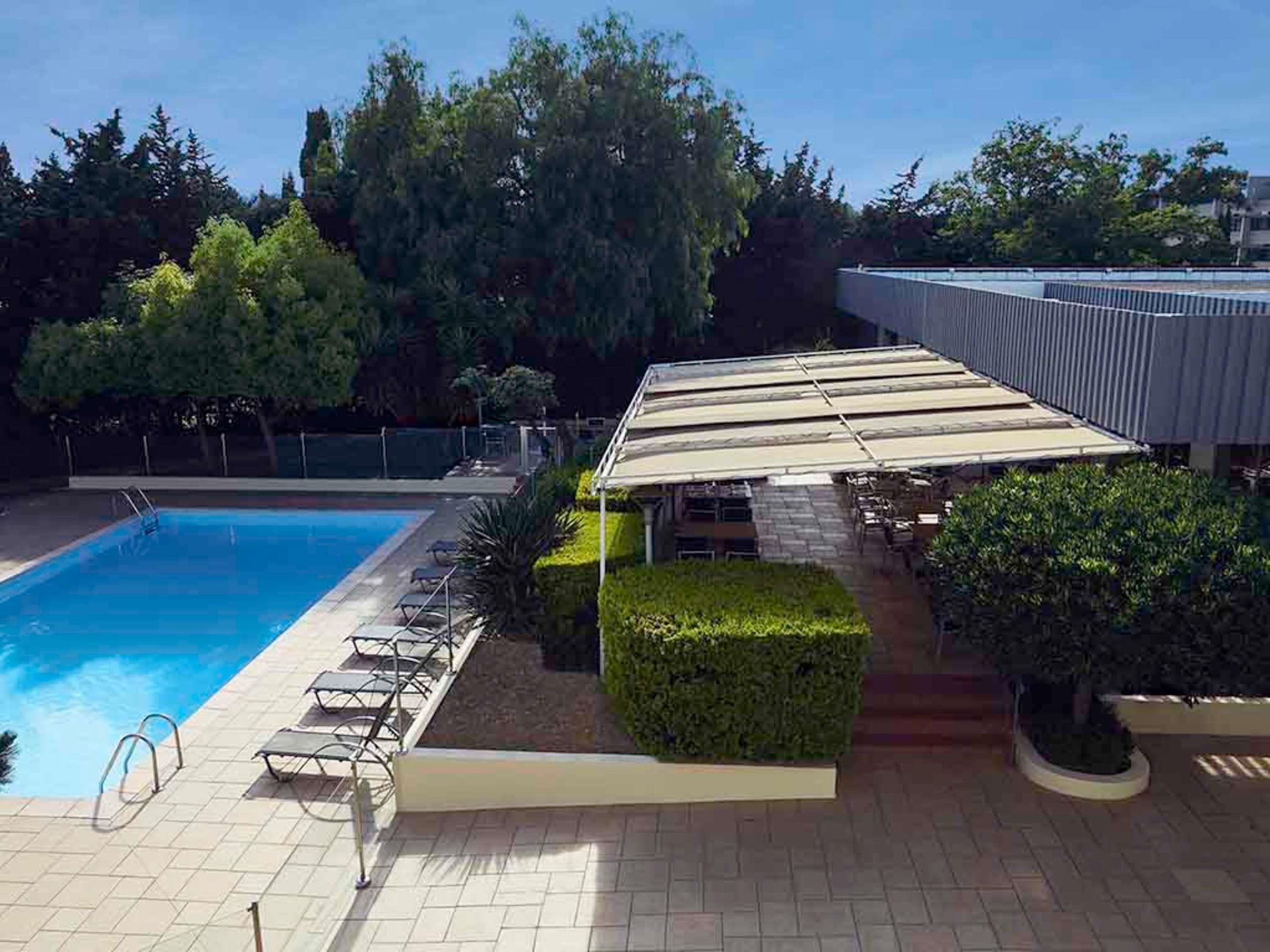 Una piscina con sillones de descanso, una zona de estar cubierta y un jardín ajardinado.