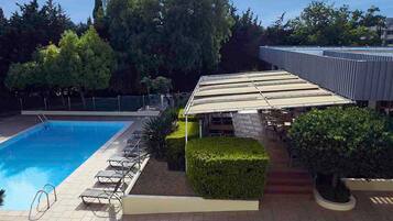 Una piscina con sillones de descanso, una zona de estar cubierta y un jardín ajardinado.