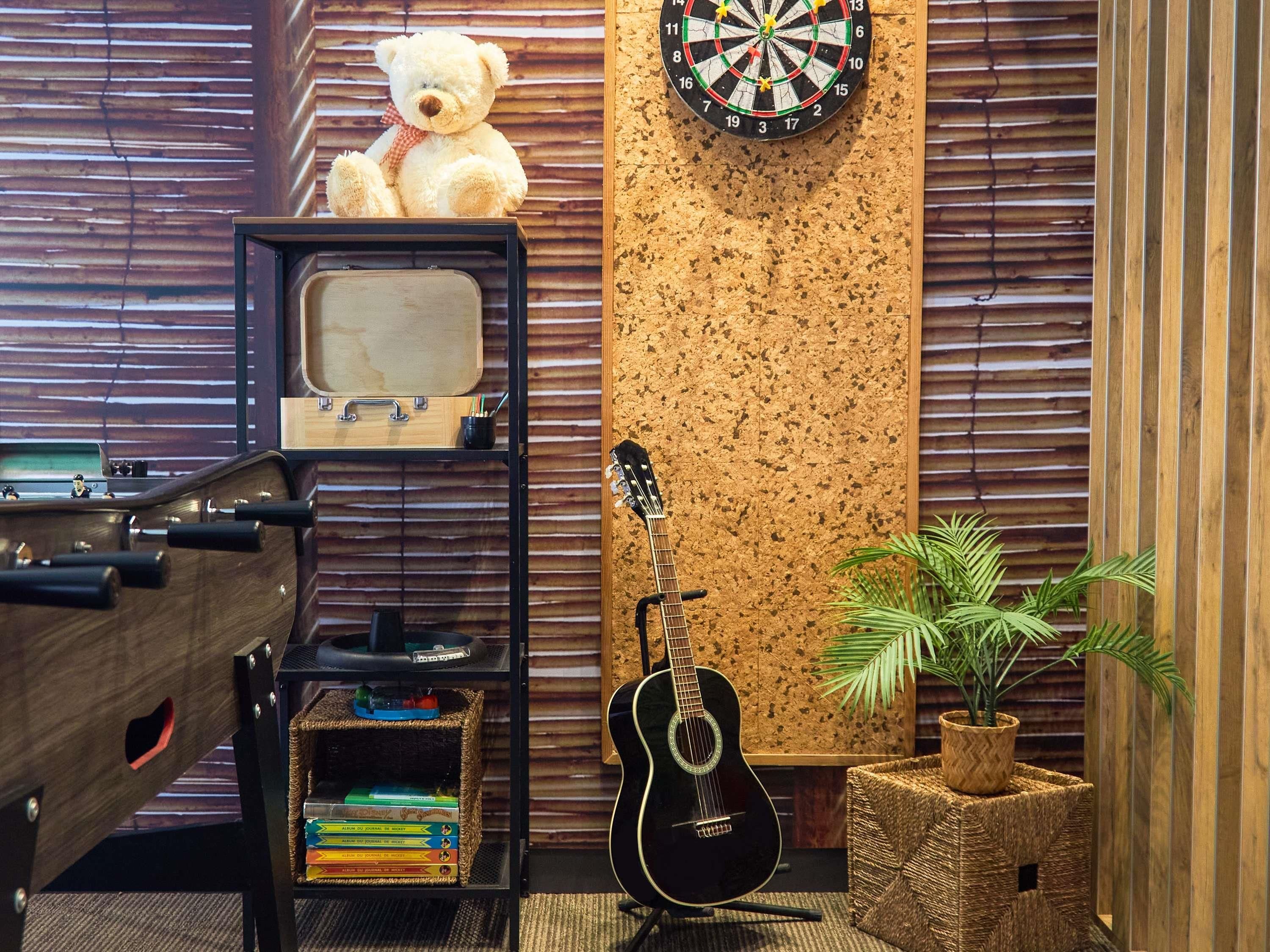 Ein Zimmer mit Gitarre, Dartscheibe, Teddybär, einem alten Fernseher und einem Bücherregal.