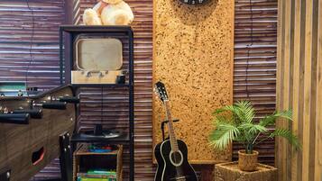 Una habitación con una guitarra, un dardo, un osito de peluche, un televisor antiguo y una estantería.