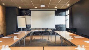 Une salle de conférence équipée d’une grande table, de chaises, d’un écran de projection et d’un tableau blanc.