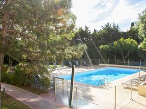 A swimming pool with a glass barrier, surrounded by trees and lounge chairs.