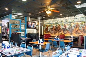 A restaurant with booths and tables, a ceiling fan, and a mural on the wall.