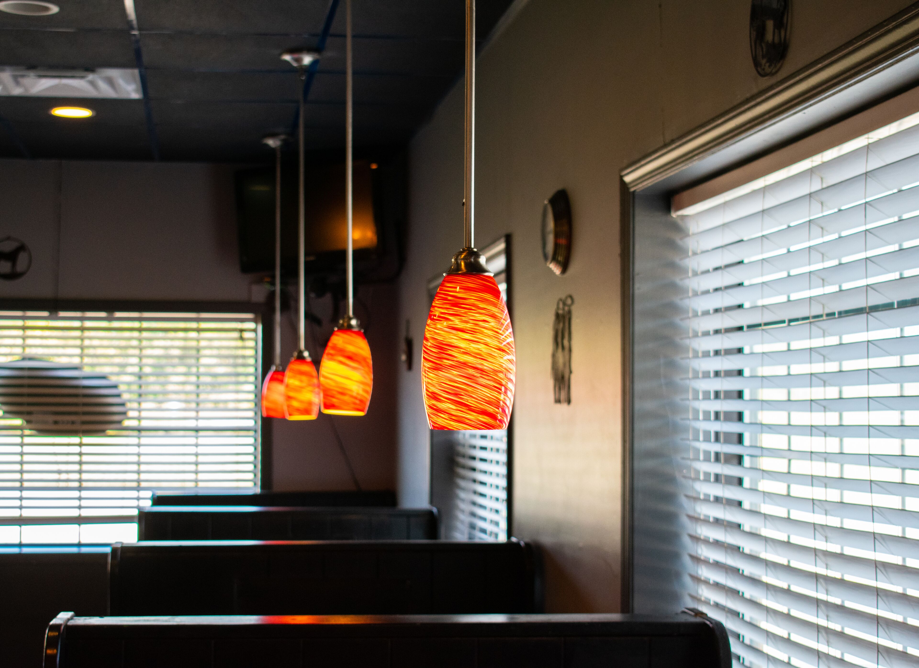 Ein Restaurantinneres mit hängenden Pendelleuchten, einem Fenster mit Jalousien und einer Wanduhr.