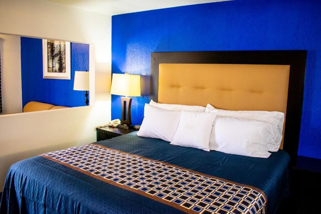 Habitación de hotel con una cama grande, cabecera, mesita de noche, lámpara y un cuadro en la pared.