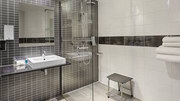 Un baño moderno con cabina de ducha de vidrio, un lavamanos blanco y un taburete pequeño.