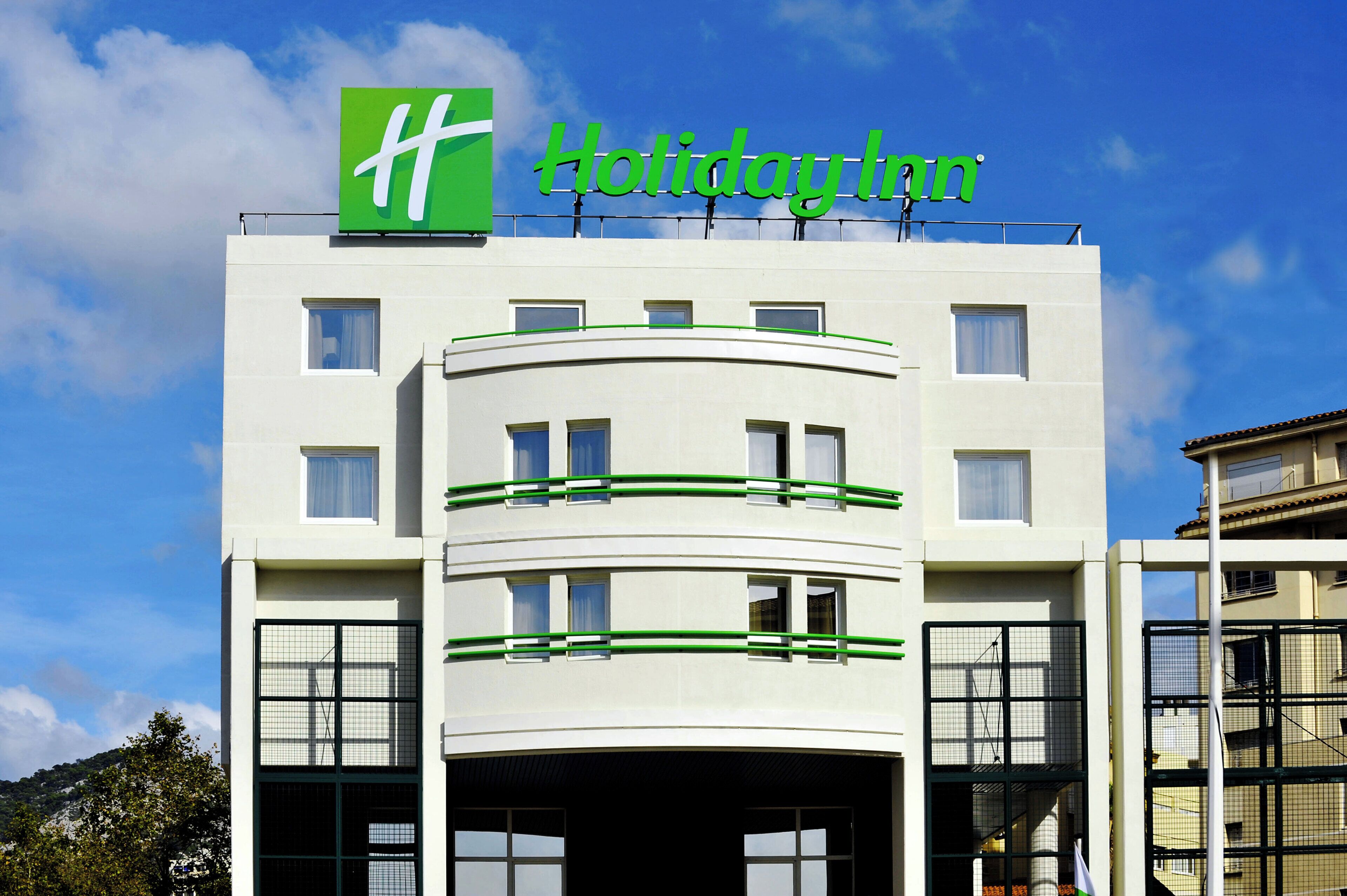 Een Holiday Inn hotelgebouw met een opvallend groen logo, meerdere ramen en een gebogen gevel.