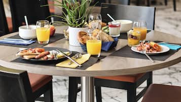 A breakfast setting with a table set for two, including plates of food, glasses of orange juice, and a bowl of cereal.