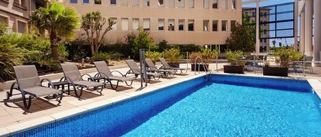 Una piscina con sillas de descanso y un edificio al fondo.