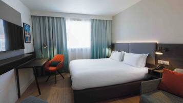 A hotel room with a large bed, a desk with a chair, a TV, and a window with curtains.