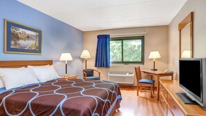 Una camera d'albergo con un letto, due poltrone, una scrivania con televisore, una finestra con tende e un quadro appeso al muro.
