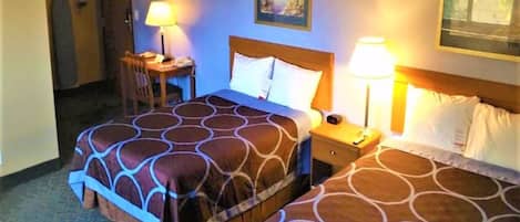 Habitación de hotel con dos camas, cada una con una colcha estampada, lámparas de noche, una mesita y una silla.