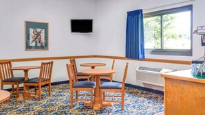 Una camera d'albergo con un angolo relax, una TV a schermo piatto montata a parete, una finestra con tende blu e un tappeto decorato.
