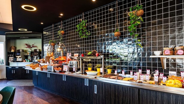 Un mostrador de buffet con diversos alimentos y una pared de azulejos con plantas colgantes.