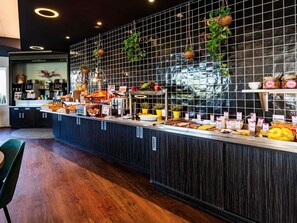 A buffet counter with various food items and a tiled wall with hanging plants. - Novotel Reims Tinqueux (Tinqueux)
