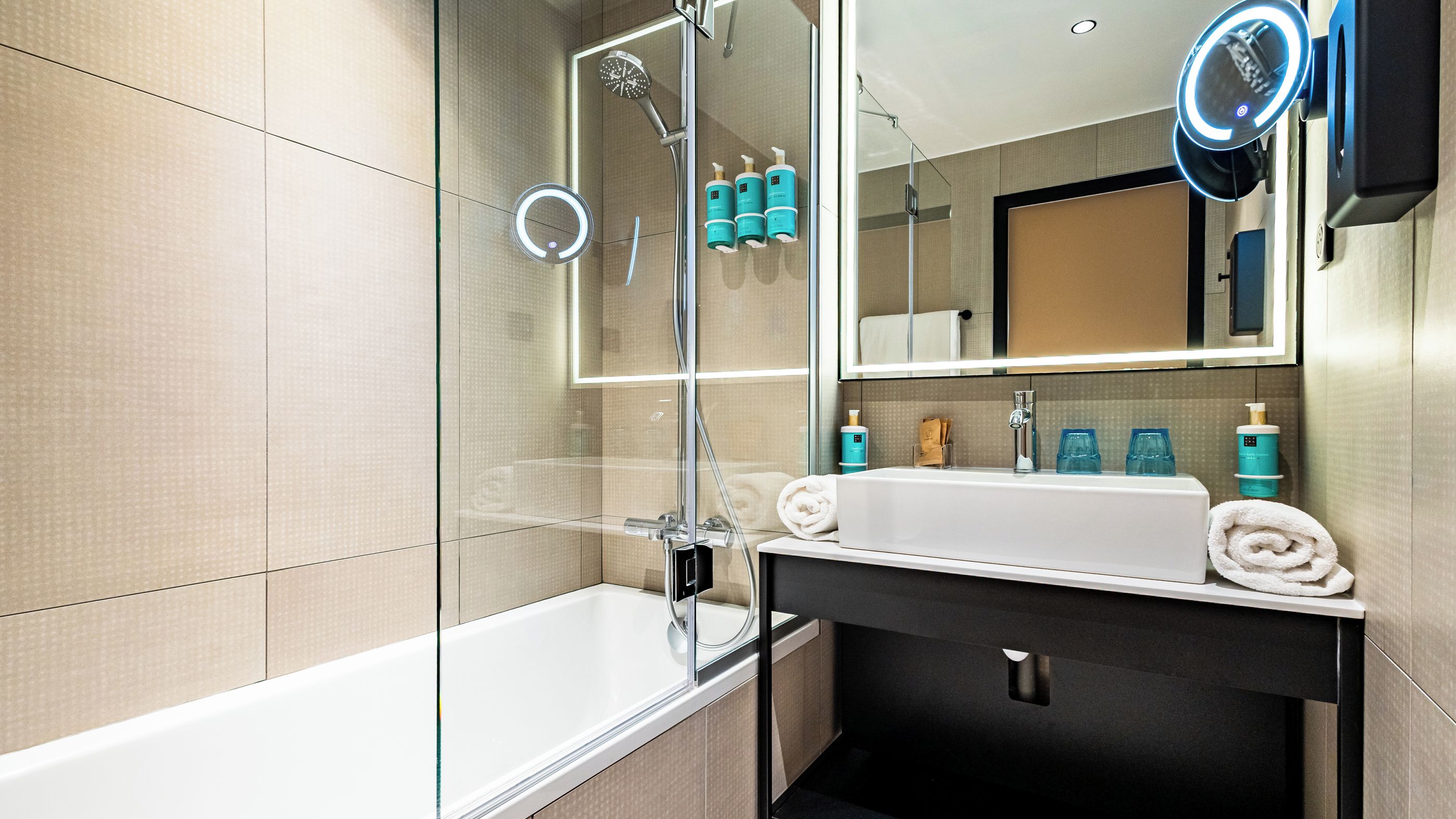 A modern bathroom with a glass-enclosed shower, a white sink, and a mirror with a built-in light.