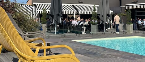 A poolside area with yellow lounge chairs, a pool, and a building with striped awnings in the background.