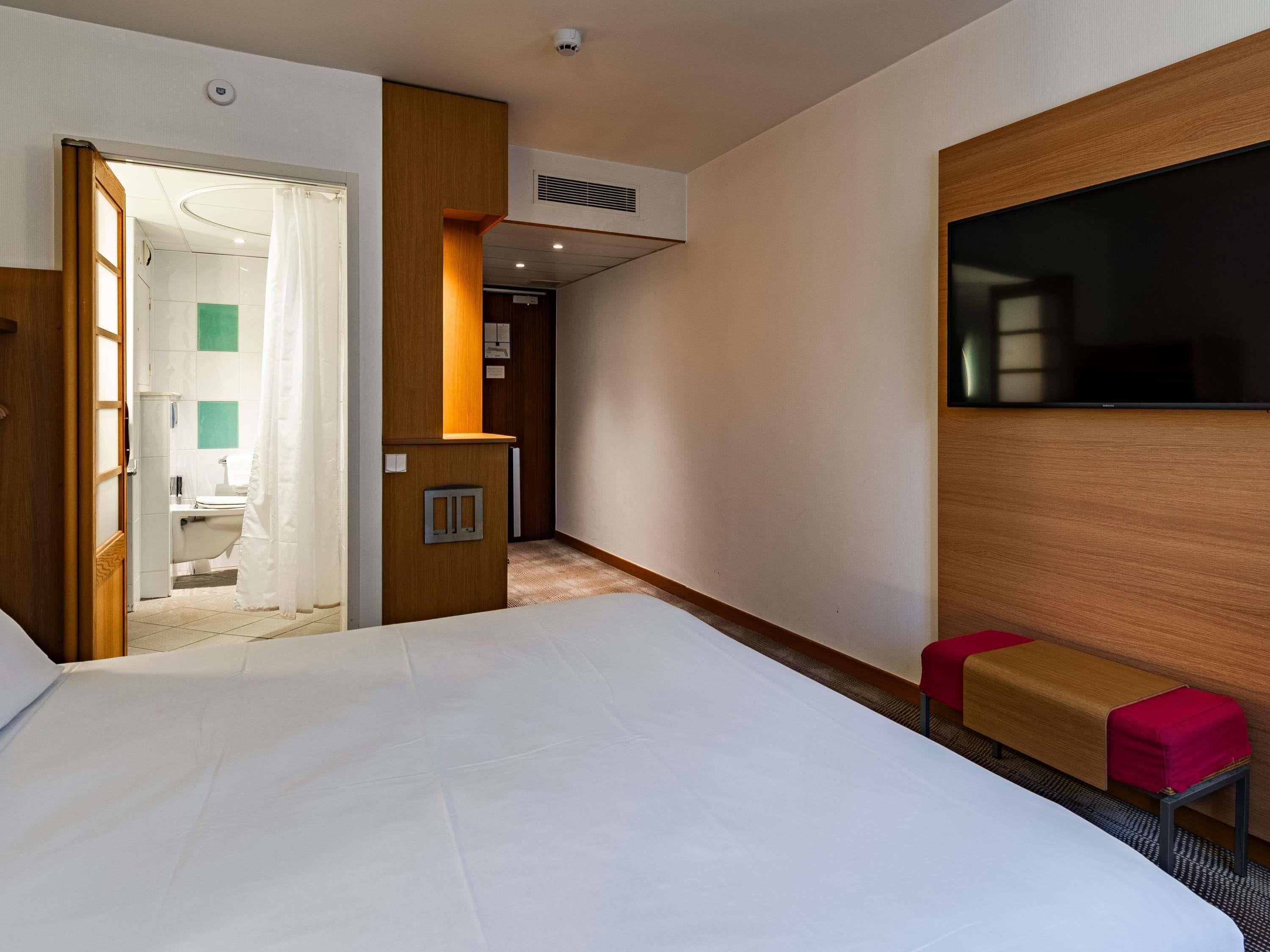 Une chambre d’hôtel avec un grand lit, une télévision, un petit coin salon et une salle de bain visible à travers une porte ouverte.