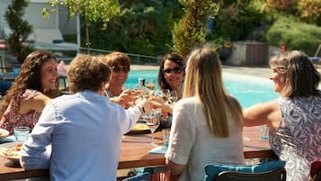 A group of people seated around a wooden table outdoors, with a pool in the background.