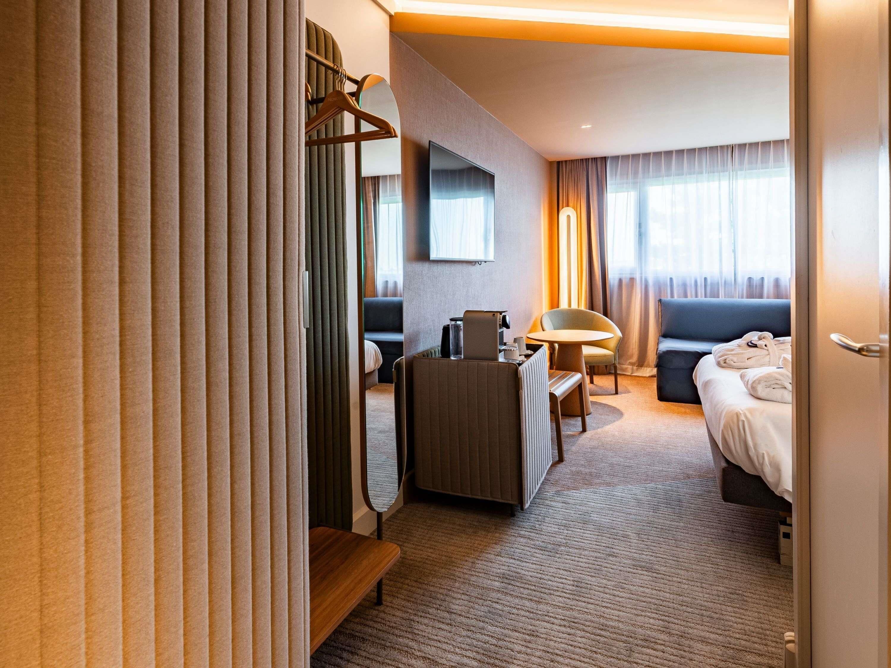 Habitación de hotel con cama, escritorio, silla, sofá, televisor y espejo.