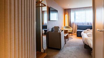 Habitación de hotel con cama, escritorio, silla, sofá, televisor y espejo.