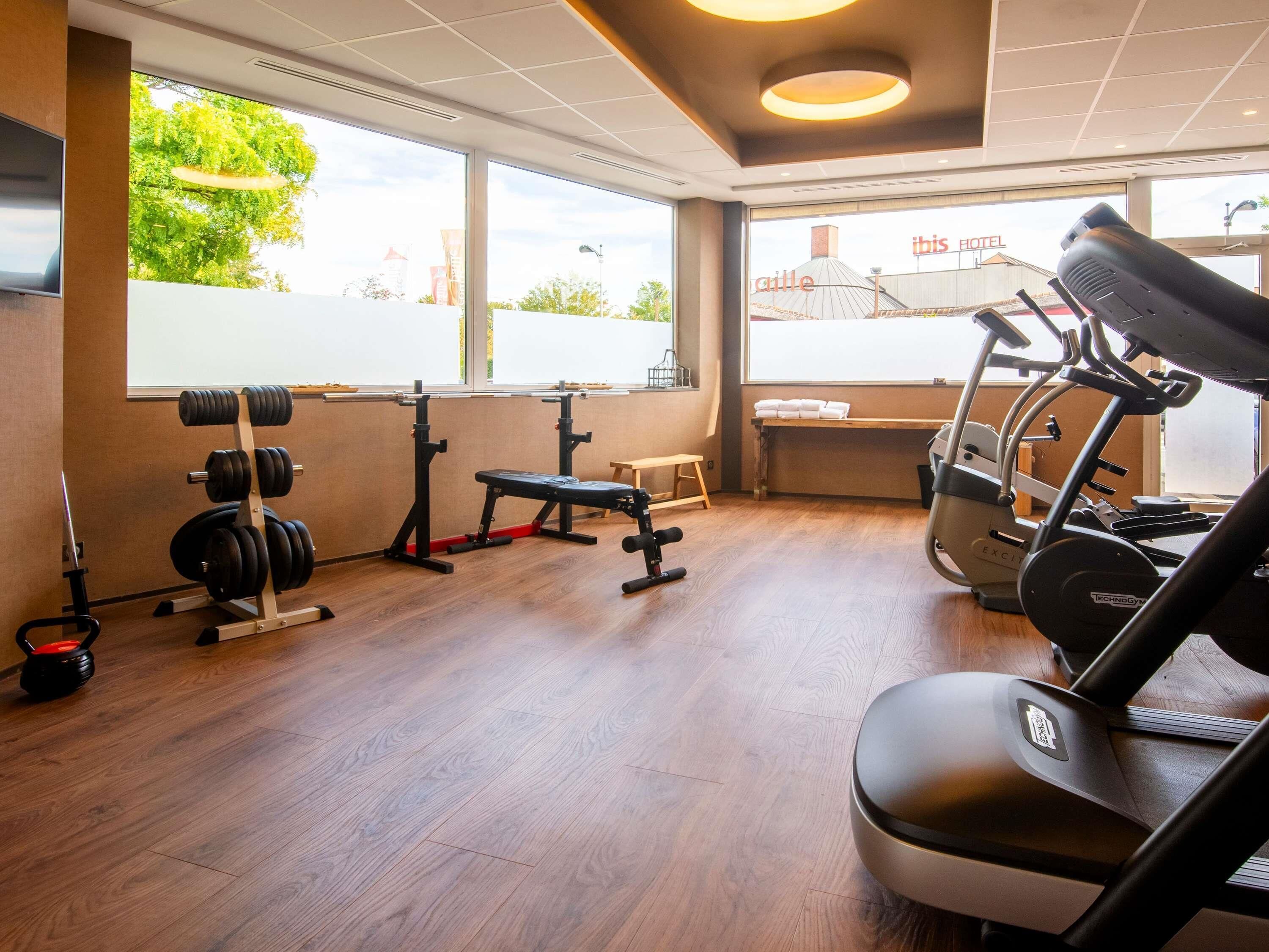 Uma academia com equipamentos de ginástica, um banco e amplas janelas com vista para o exterior.
