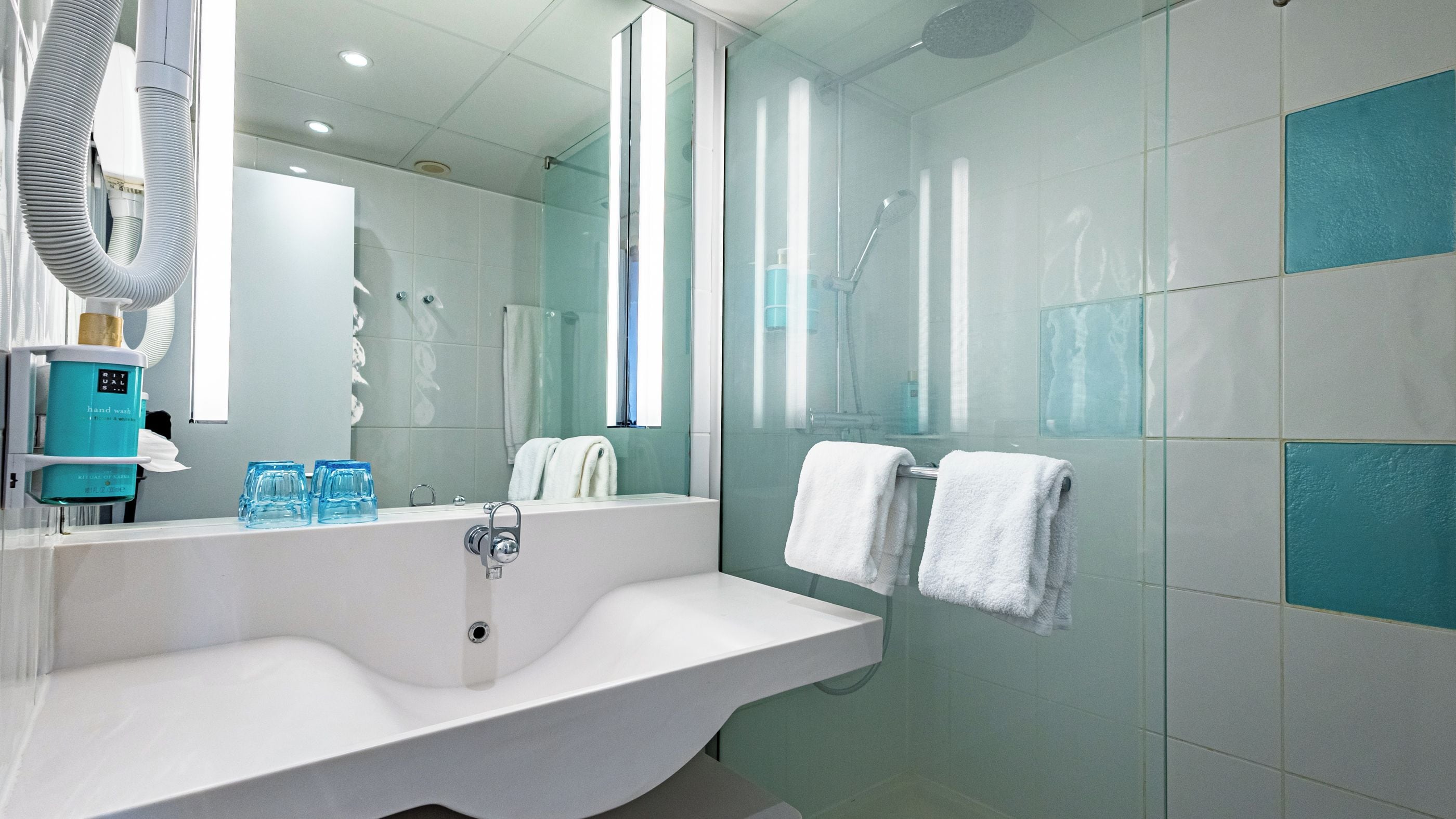 Een moderne badkamer met een ruime wastafel, een handdouche en een douchecabine met glazen wanden.