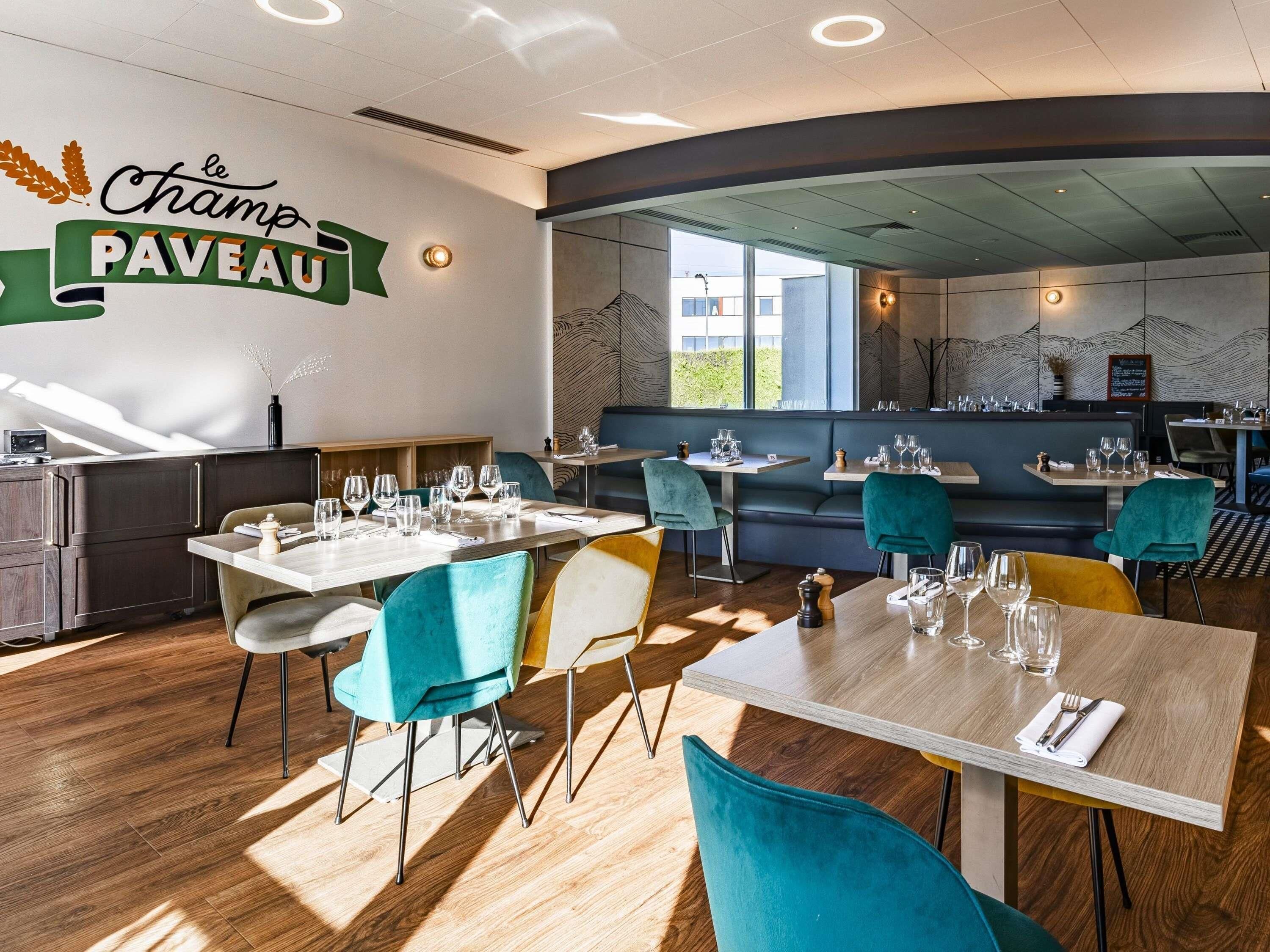 Interior de un restaurante con mesas, sillas y un letrero en la pared que dice 'le Champ PAVEAU'.