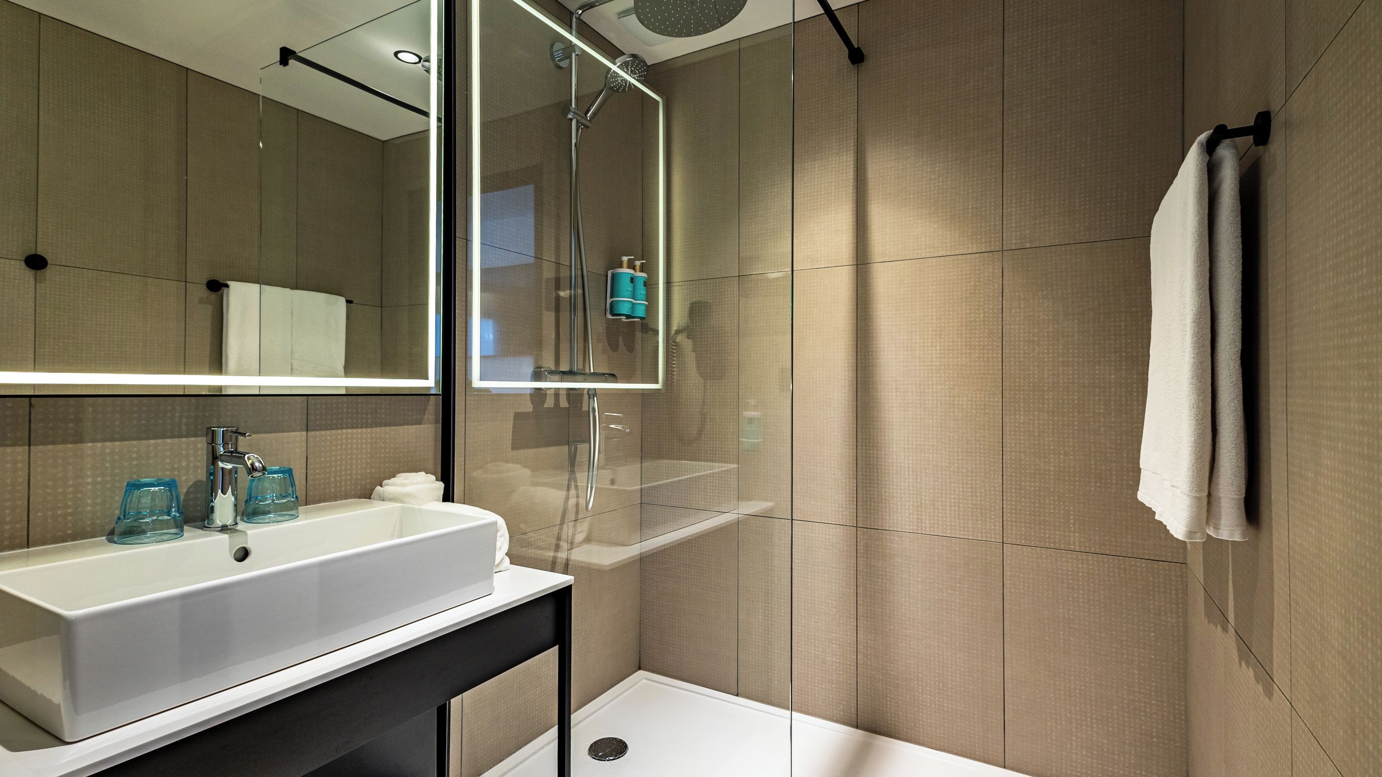 A modern bathroom with a white sink, a glass shower enclosure, and a large mirror.