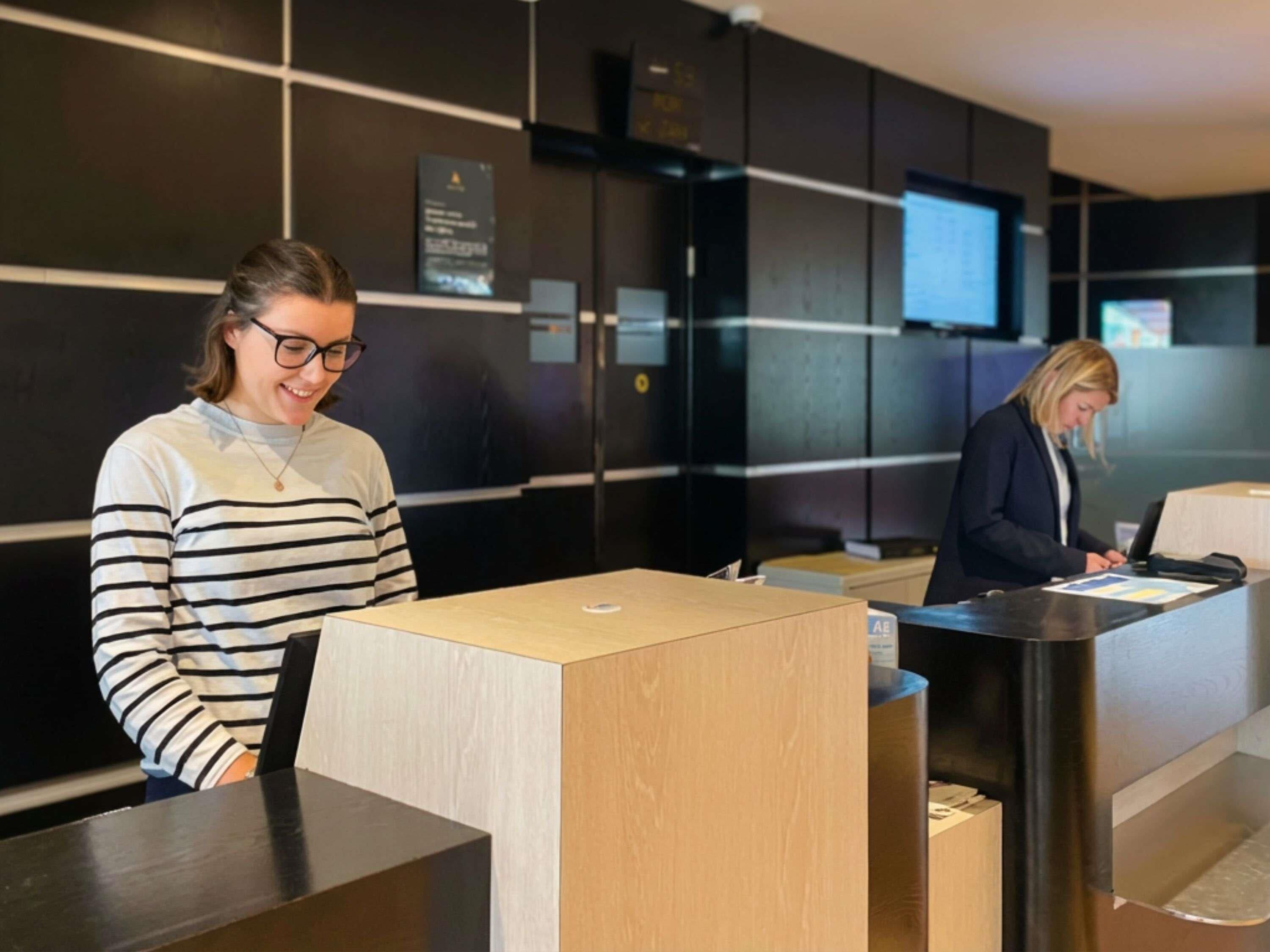 A reception desk with a wooden counter and a digital screen in the background.
