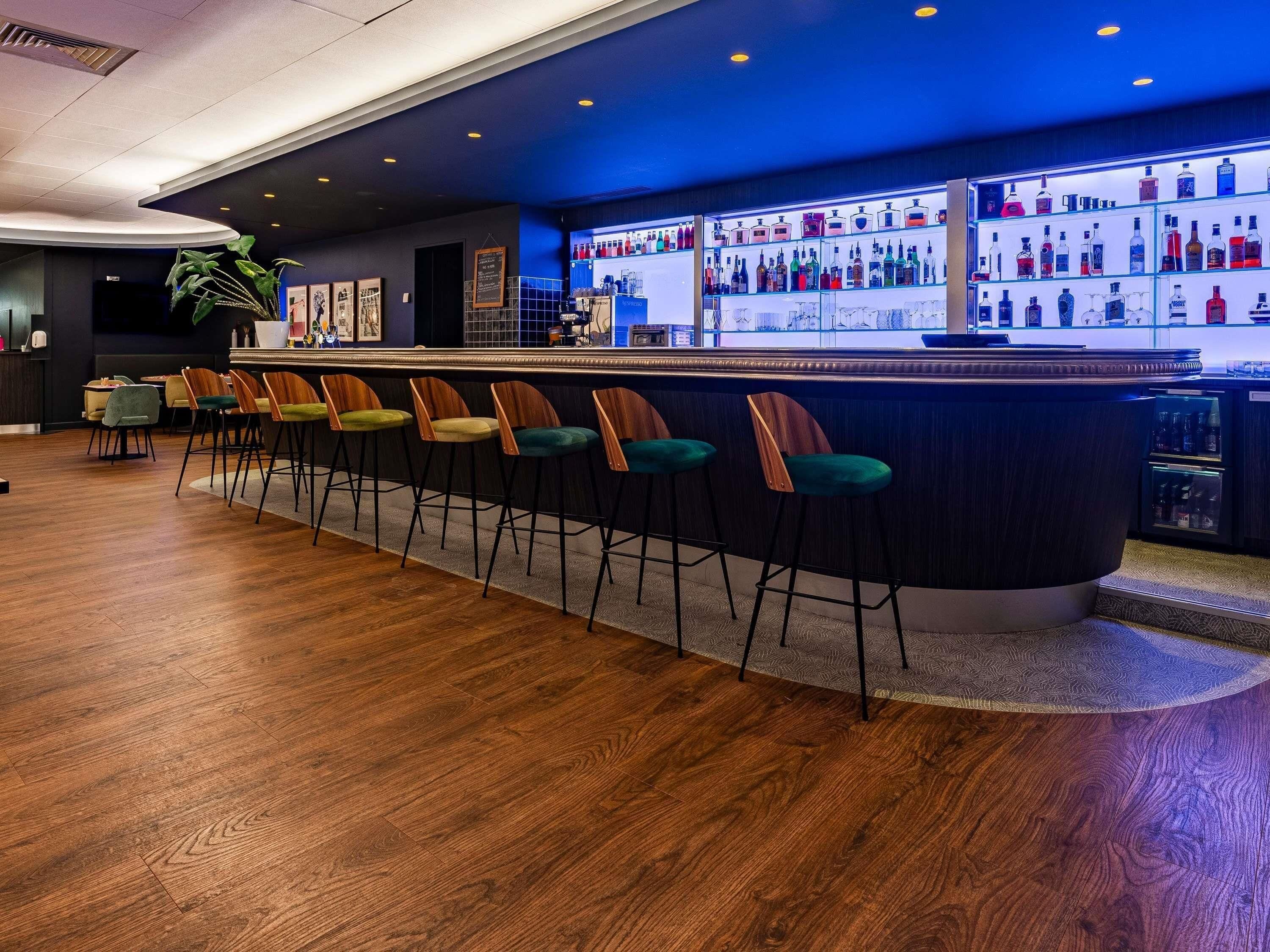 A bar area with a long counter, multiple stools, and a variety of bottles on shelves.