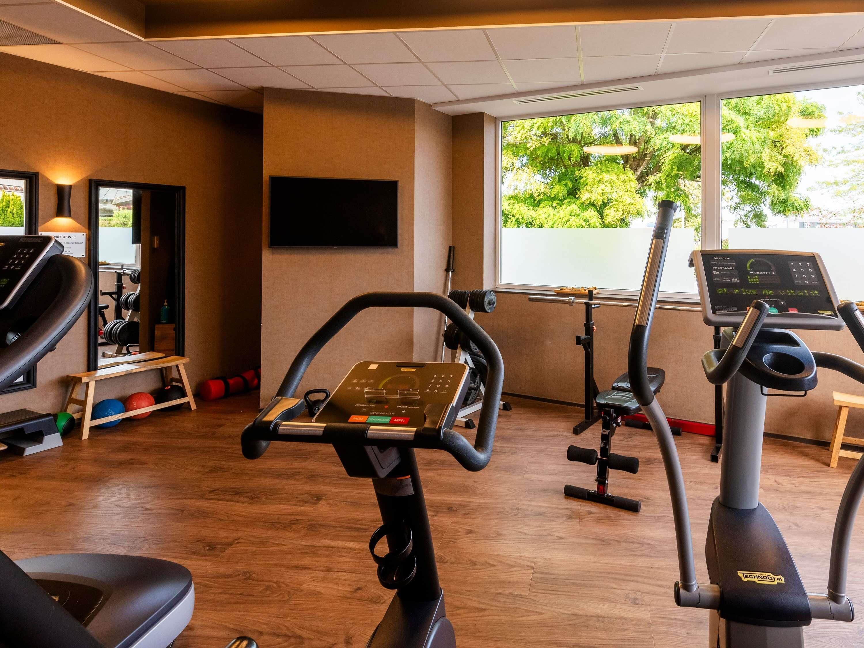 A gym with exercise equipment, a television, and a window with a view of trees.