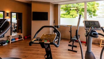 A gym with exercise equipment, a television, and a window with a view of trees.