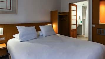 A hotel room with a large bed, a wooden headboard, a bedside table with a lamp, and a wardrobe with a mirror.
