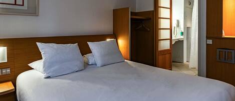 A hotel room with a large bed, a wooden headboard, a bedside table with a lamp, and a wardrobe with a mirror.