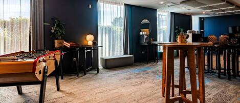 A room with a foosball table, a bar area, and a large window with curtains.