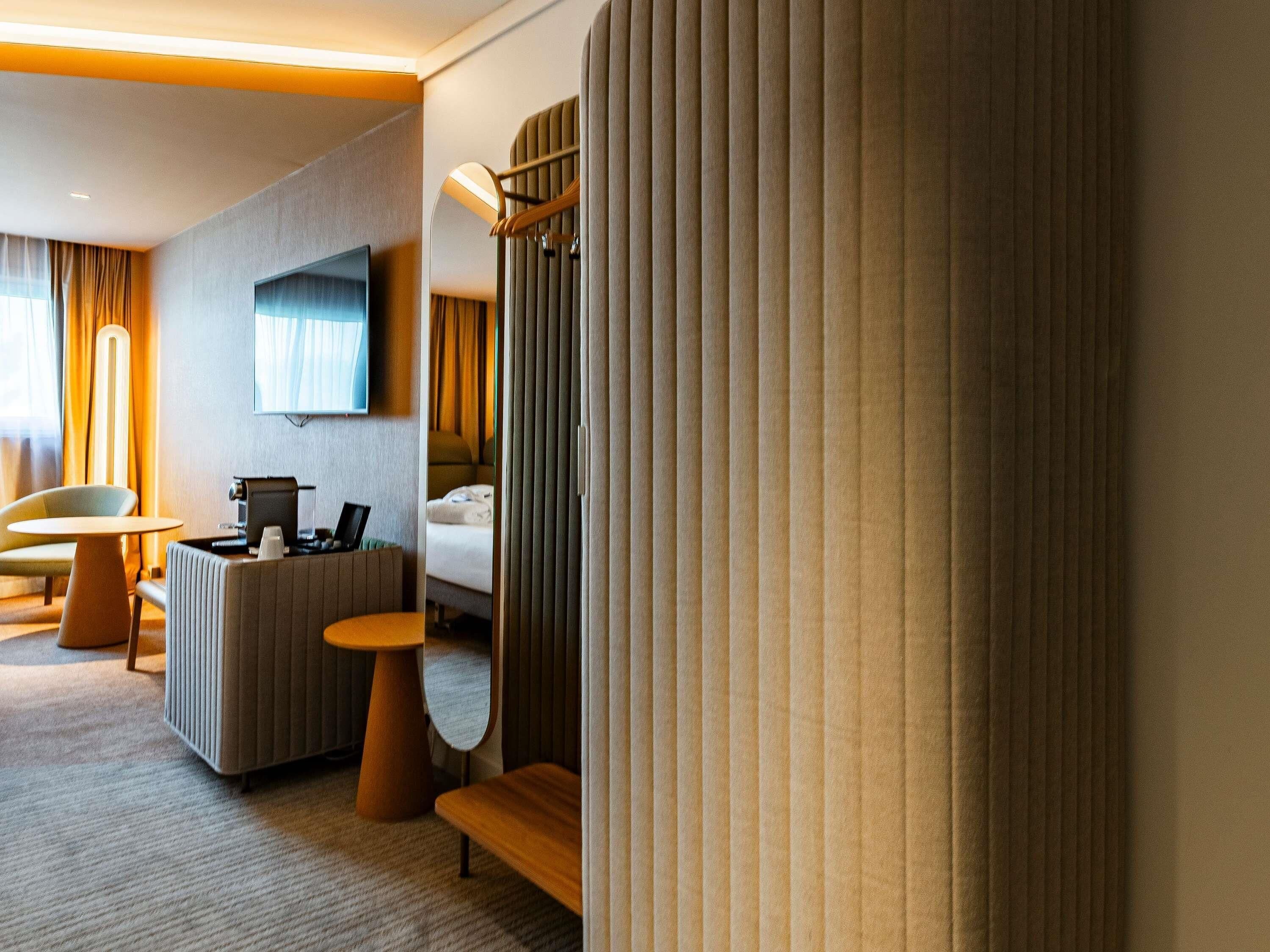 A modern hotel room with a flat-screen TV, a desk with a laptop, a comfortable sofa, and a bed.