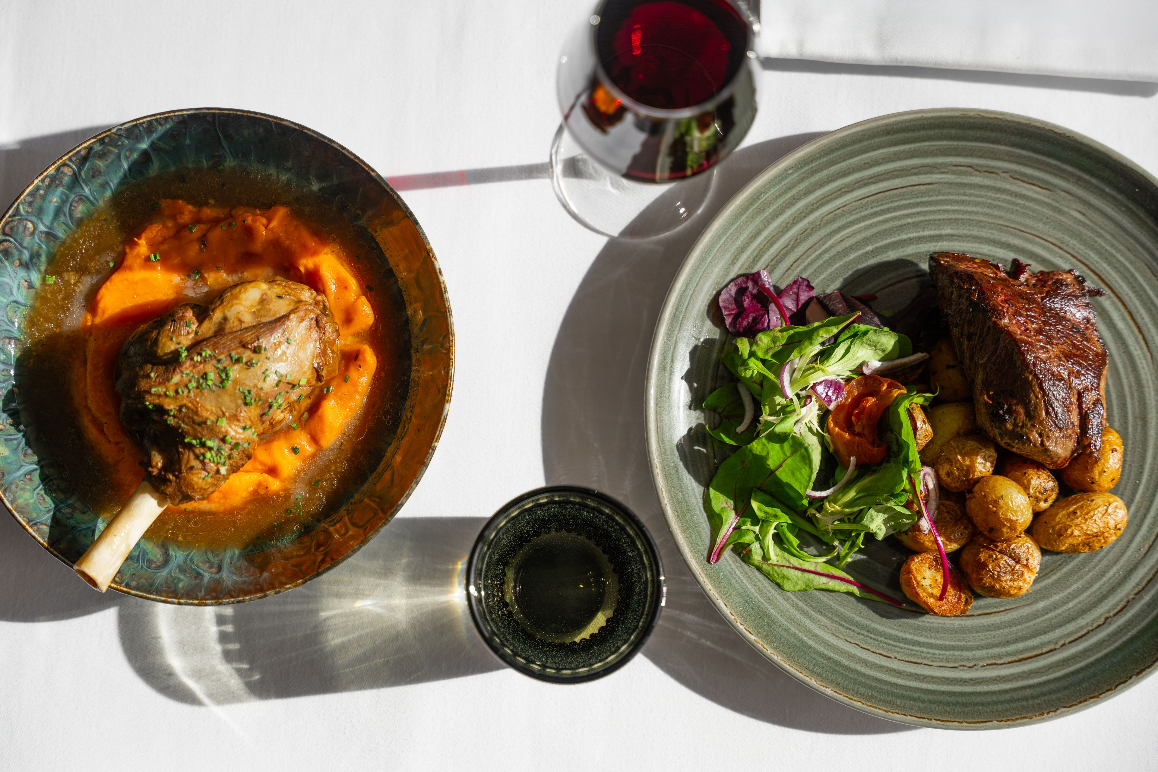 A table with a bowl of soup, a plate of salad, roasted potatoes, and a glass of red wine.